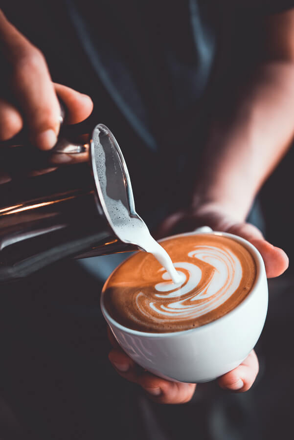 barista versant du lait dans une tasse de café