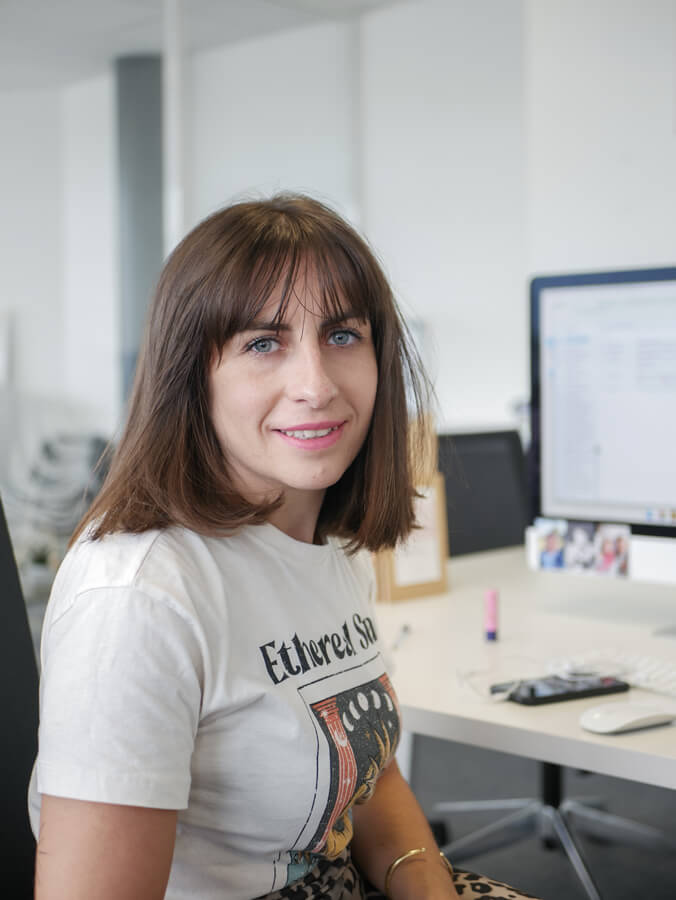 la cheffe de projet de l'agence com commerce à clermont-ferrand, souriant derrière son bureau